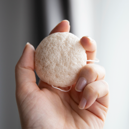 Hand holding a white konjac facial cleaning sponge. 