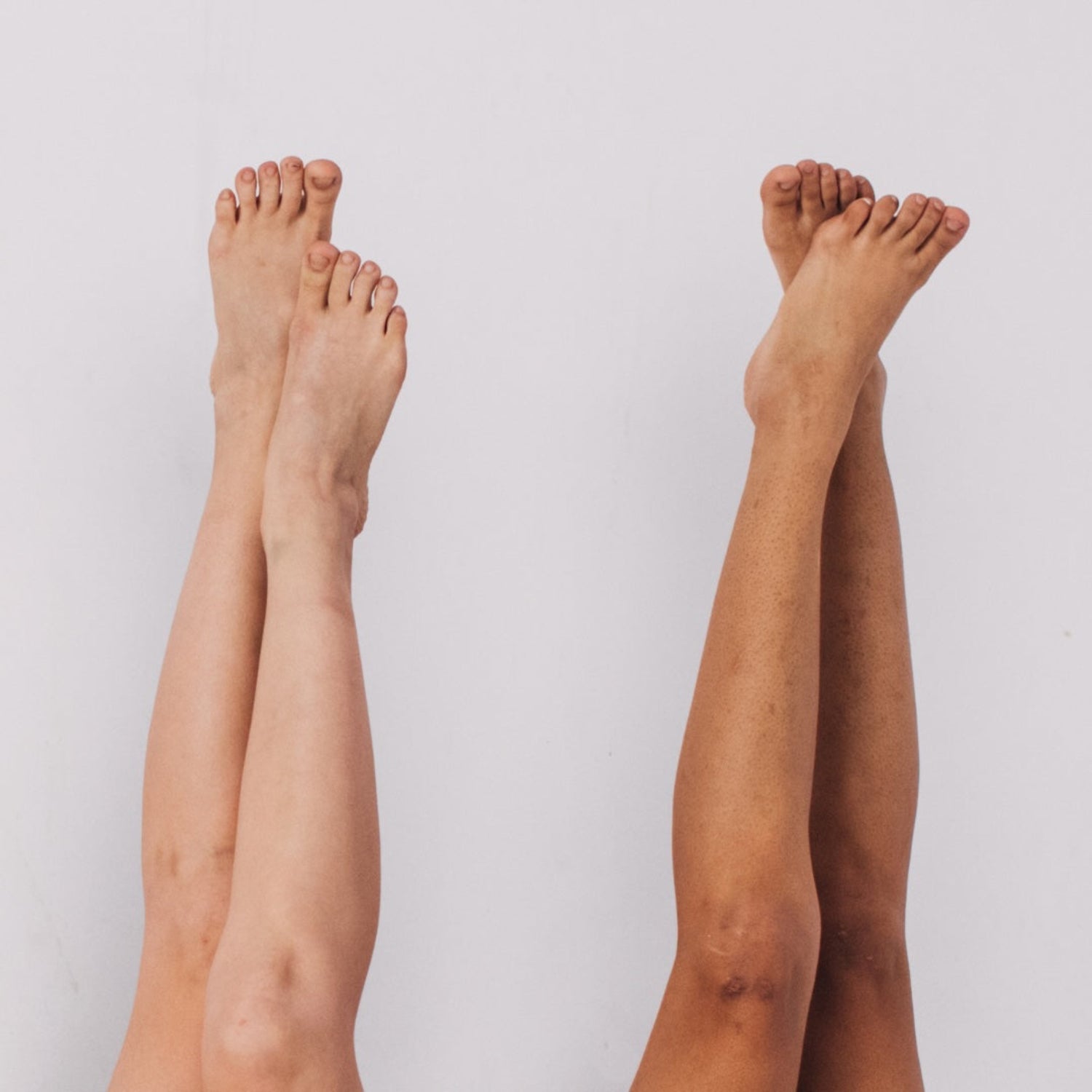 Two pairs of bare legs in waterfall pose, legs up a white wall.