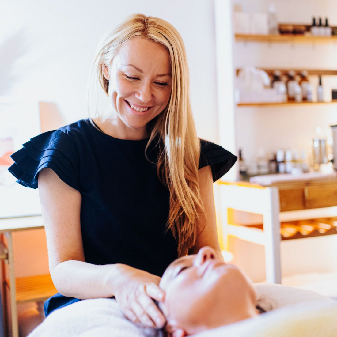 Holistic facialist smiling as she gives a facial massage in a brightly lite therapy room. 