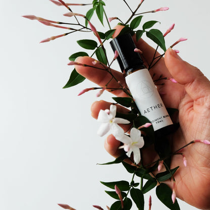 Chantals hand holder a sprig of blossoming jasmine and a bottle of aether blend. 