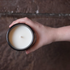 An aerial view of an open soy wax candle in an amber glass jar, held by a hand in front of a brown brick surface.