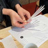 Sample sticks of essential oils being held together to create a bespoke scent recipe within a workshop setting. 