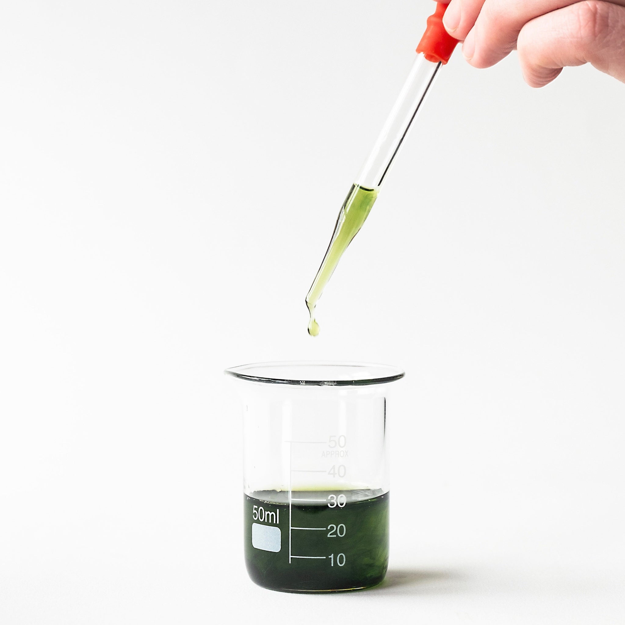 A glass dropper of blue chamomile essential oil being dropped into a glass beaker. 