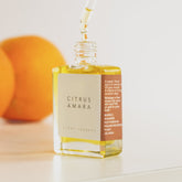 An open bottle of citrus Amara scent therapy blend with dropper top and oranges in the background. 