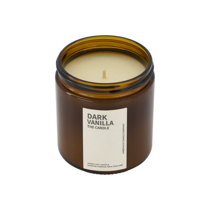 A large amber glass jar with brass lid containing dark vanilla candle on white background. 