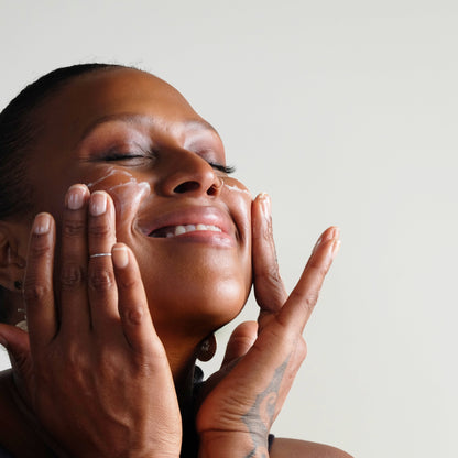 Deva smiling with her eyes closed as she applies face cream to her cheeks.