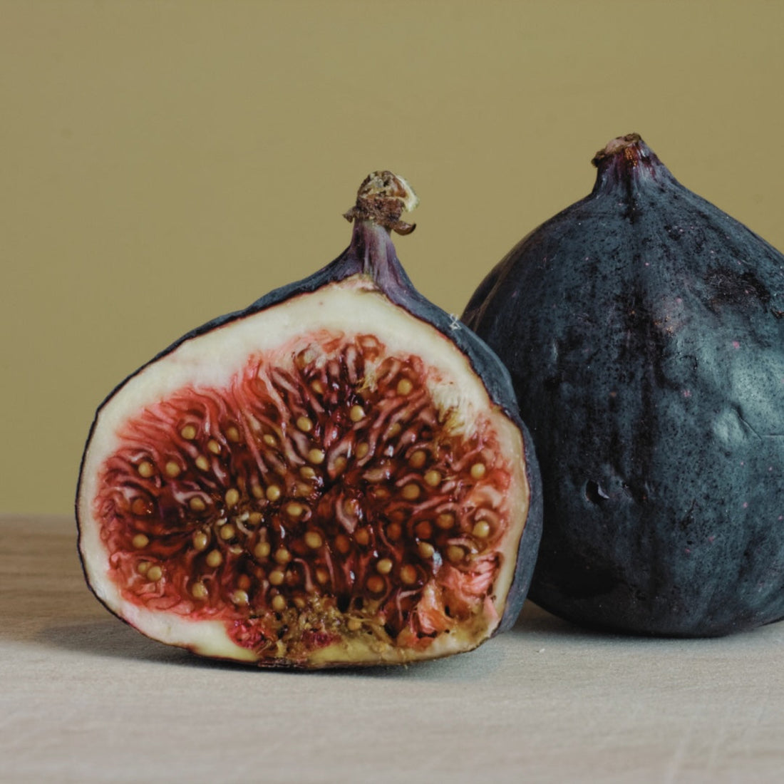 Ripe fig cut in half on cream bench and greenish beige background. 