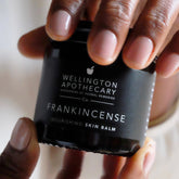 Glass jar of frankincense balm healing elegantly in hands. 