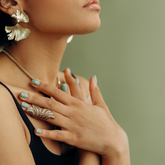 A woman with soft, smooth skin placing her hands over her chest. She has green nails and is in front of a green background. 