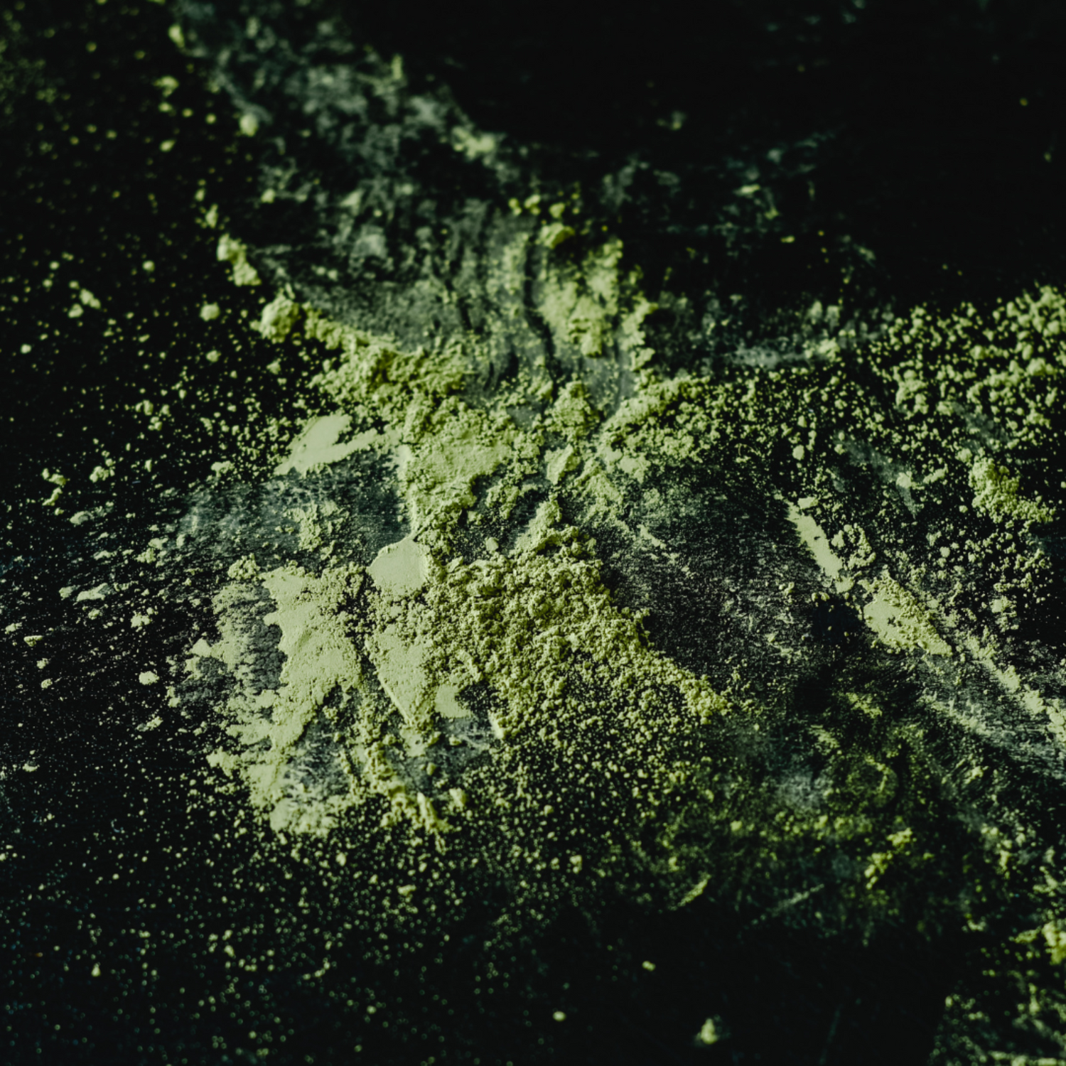 Bright green matcha powder scattered on a black surface. 