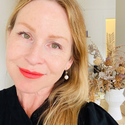 Portrait of Mel wearing red lipstick and pearl earrings, dried flower bouquet in the background. 