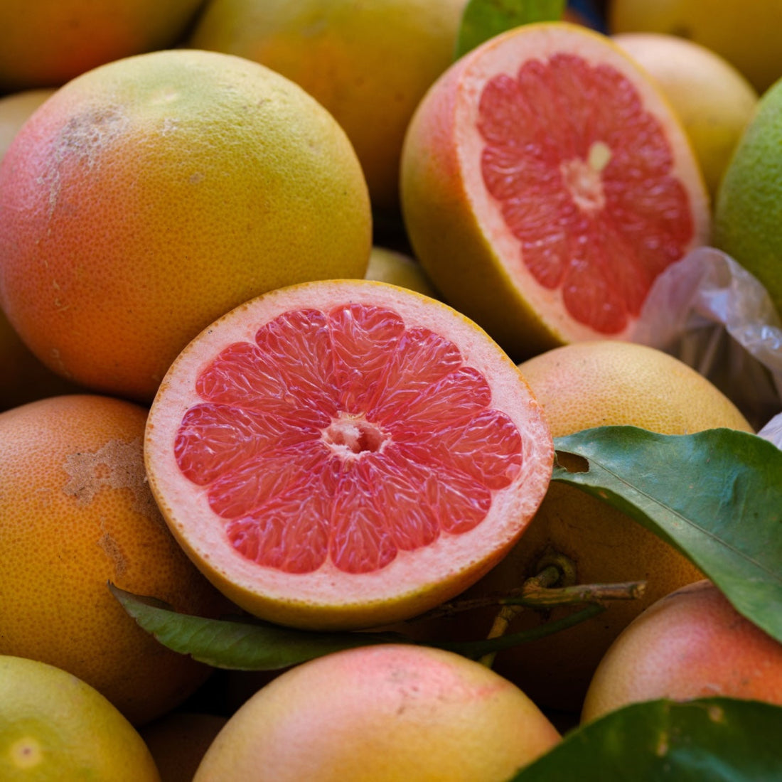 A pile of grapefruits, one sliced open with pink flesh inside. 