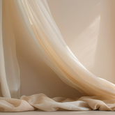 A creamy coloured silk curtain strewn across a creamy wall and over the floor in soft sunlight. 