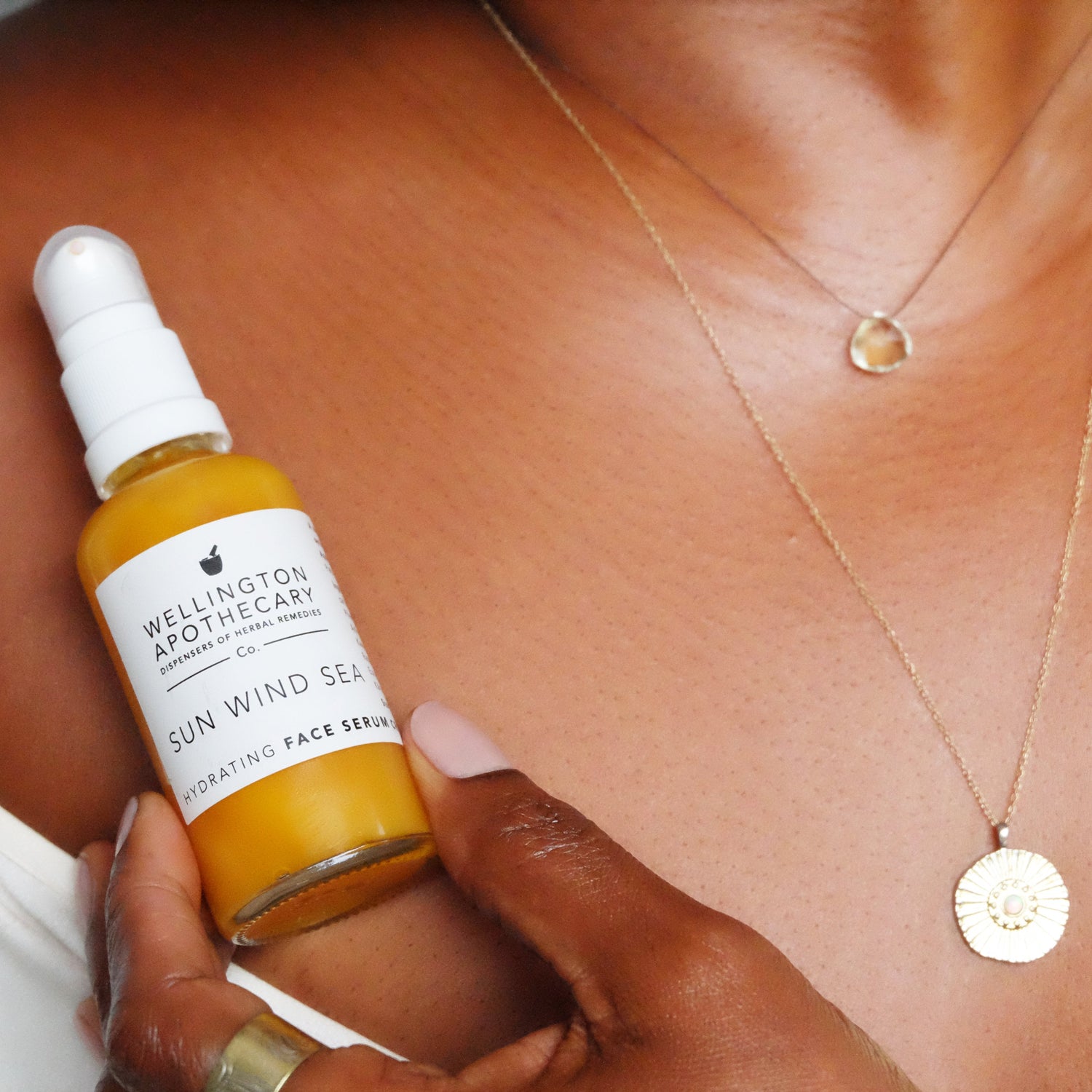 Glass bottle of honey coloured serum held in front of bare shoulder with glowing, shimmering skin. 