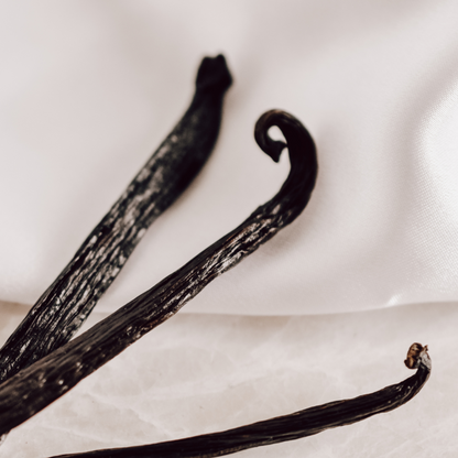 Three vanilla beans on white silk.