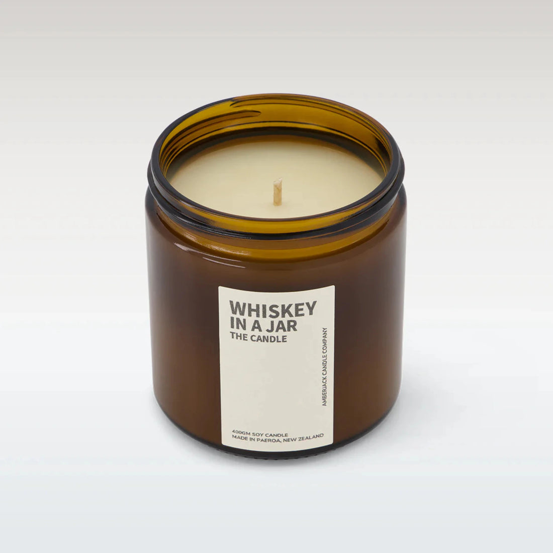 A large amber glass jar containing whiskey in a jar candle on white background. 