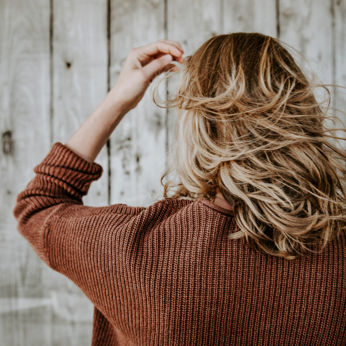 Woman wearing a cinnamon coloured jumper, her blonde glossy, textured hair swept by the wind. 