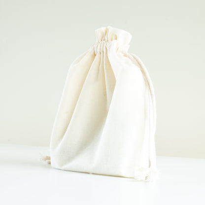 Natural calico drawstring bag on white bench and soft cream background. 