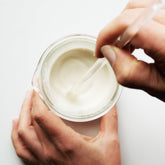 Ivory clay being mixed into a past within a beaker on white surface.