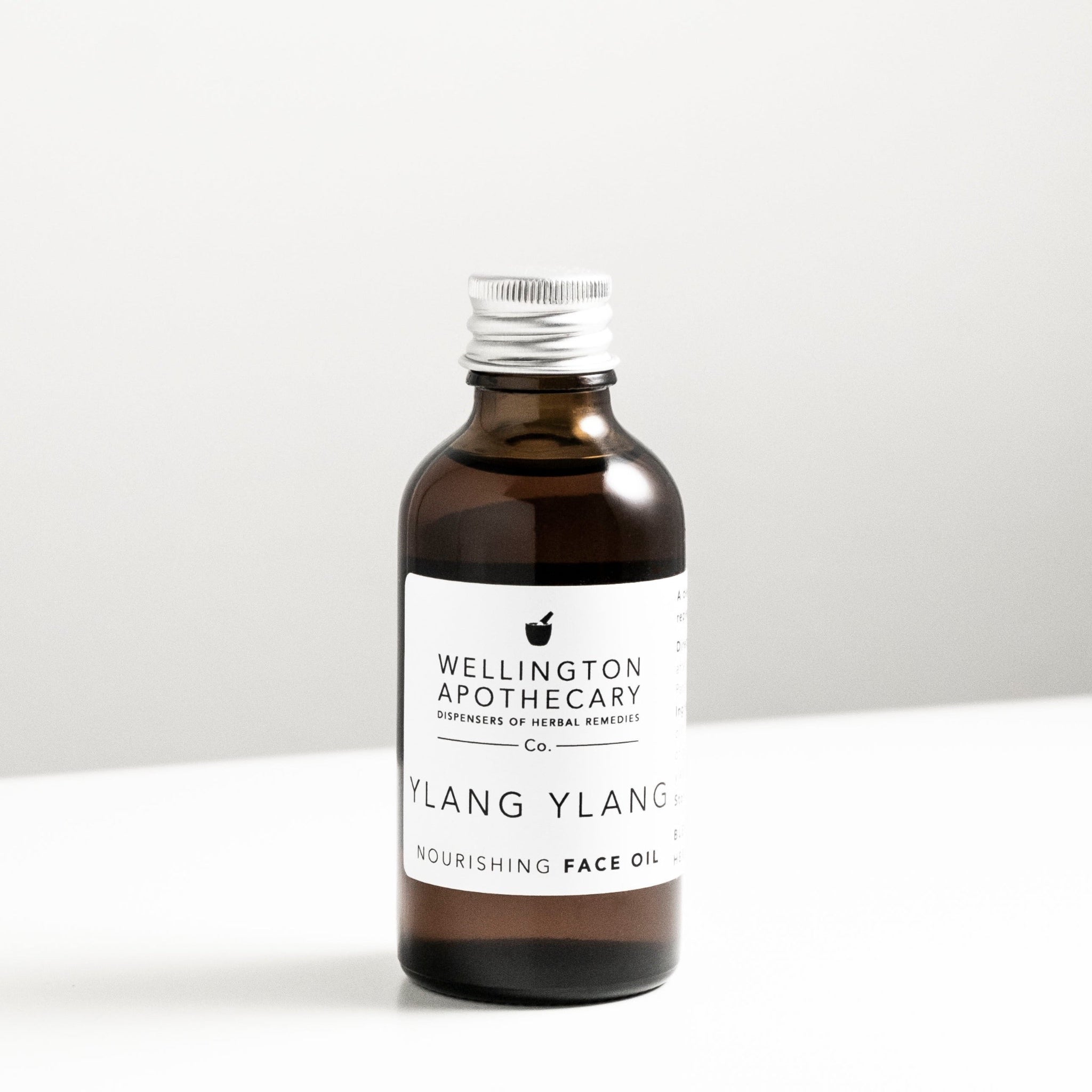 Amber glass bottle with aluminium lid on white bench. White Wellington Apothecary label - Ylang ylang nourishing face oil. 