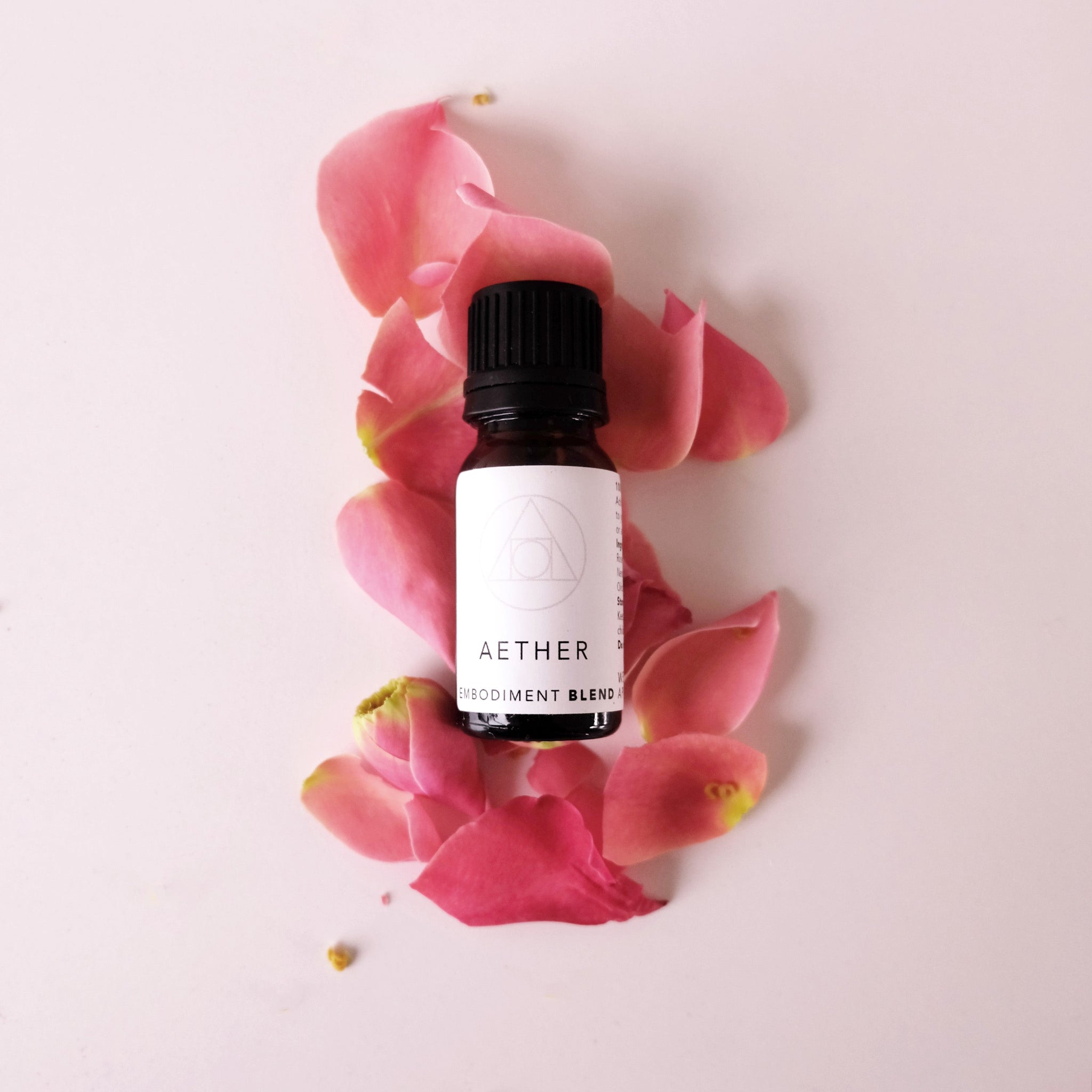 Small amber glass bottle of aether essential oil blend lying on fresh pink rose petals.