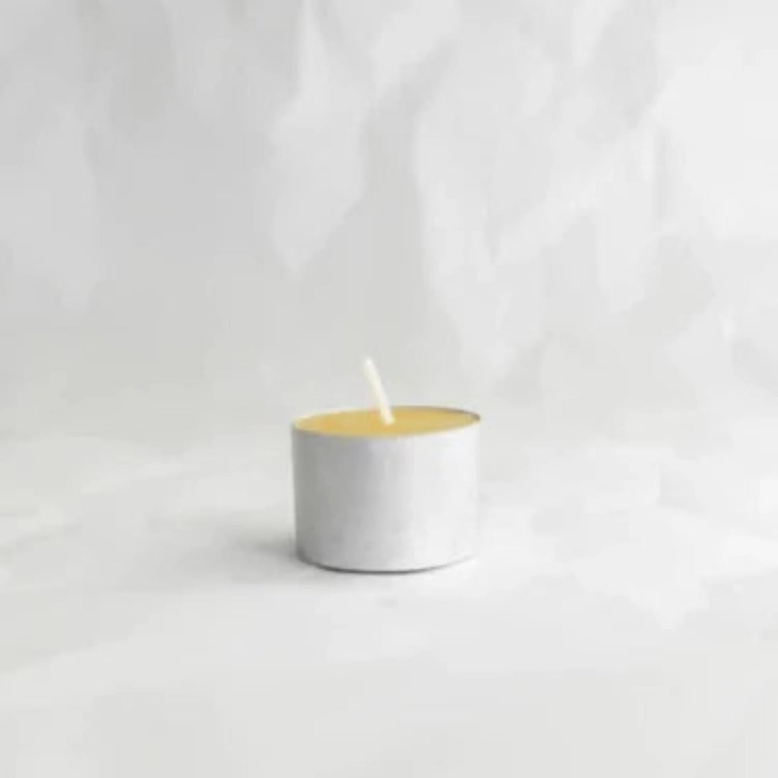 A single beeswax tea light candle on white background.