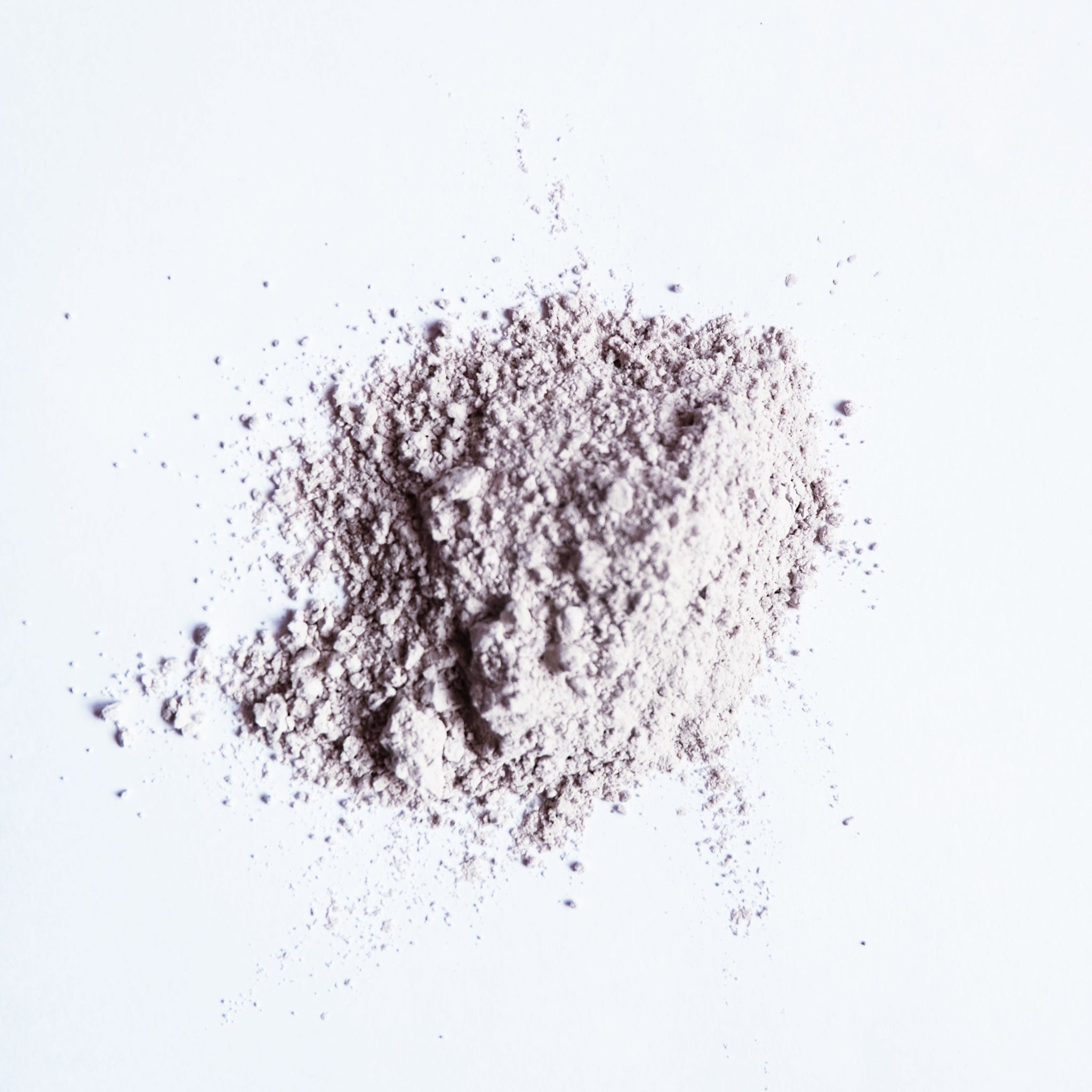 A small pile of grey bentonite clay powder on white surface. 