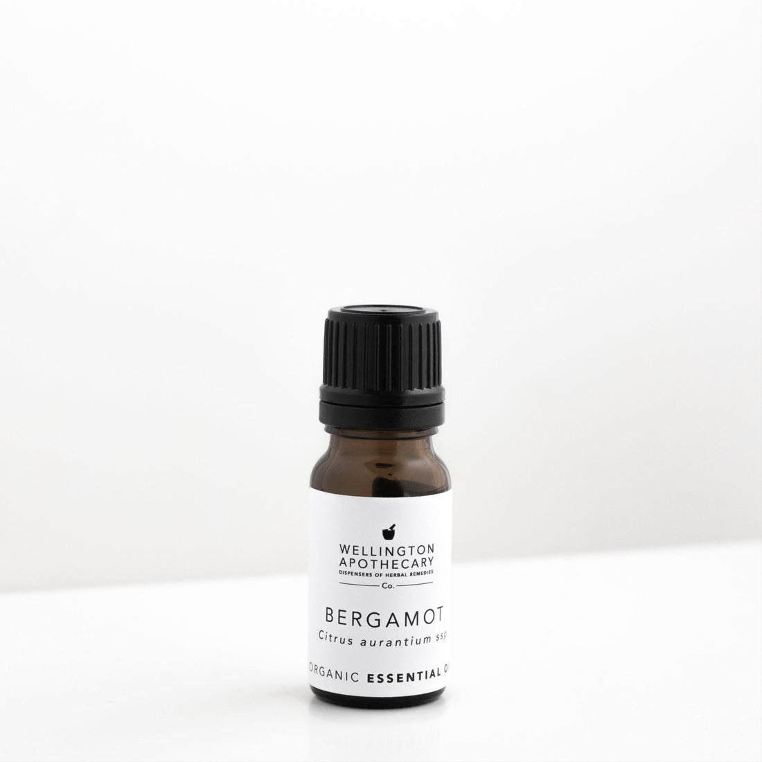 Small amber glass bottle of bergamot essential oil on white bench. 