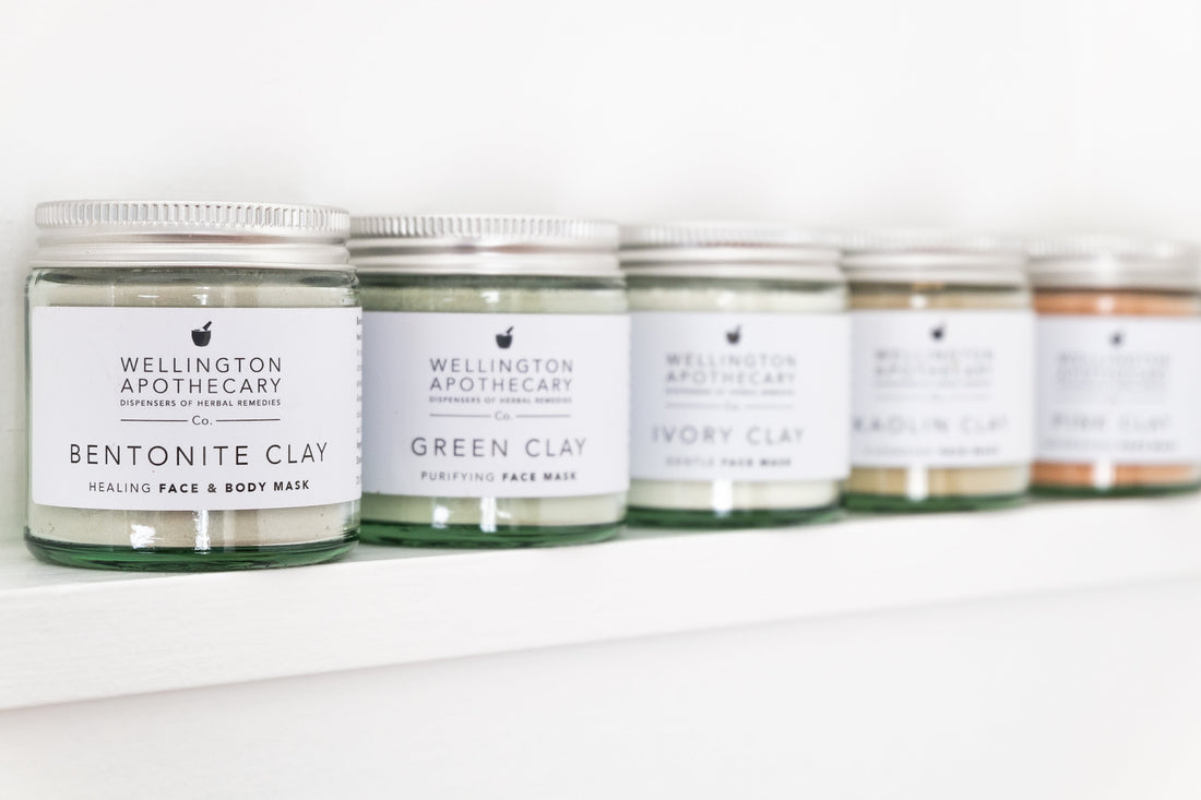 A row of jars on a white shelf filled with various coloured clay powders. 