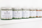 A row of jars on a white shelf filled with various coloured clay powders. 