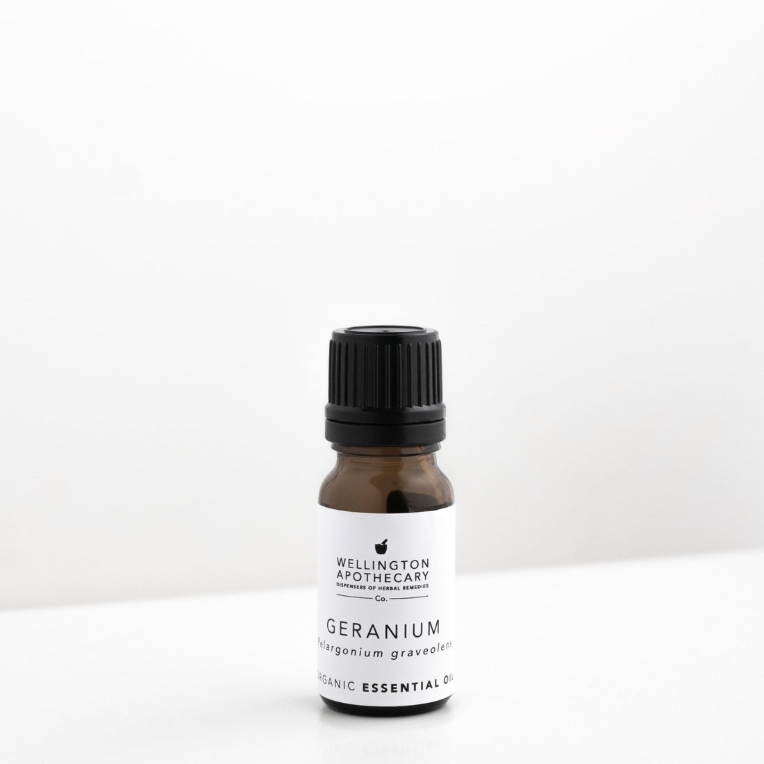 Small amber glass bottle of geranium essential oil on white bench. 