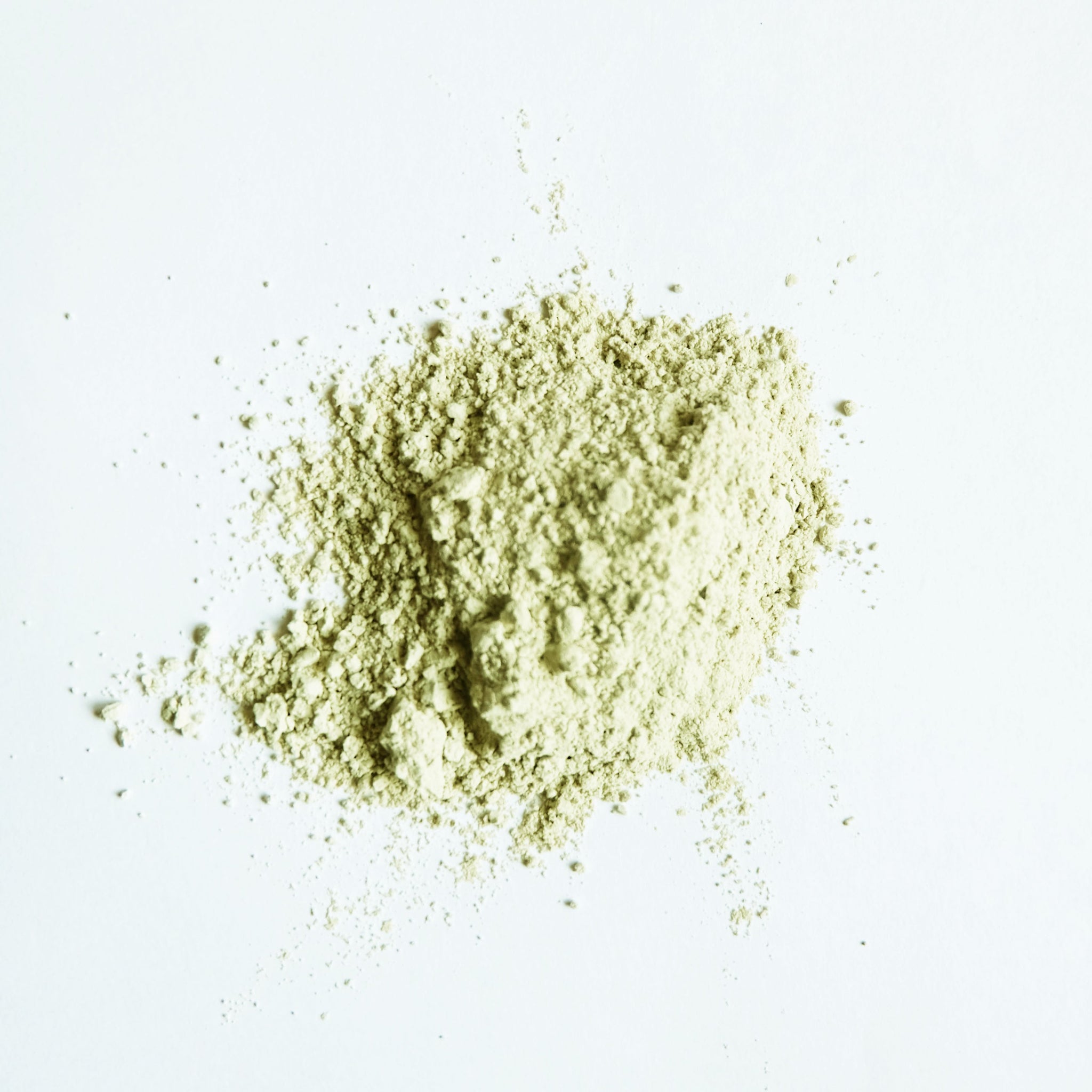 A small pile of green clay powder on white surface. 