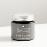 Amber glass jar of Kawakawa balm on white bench. 