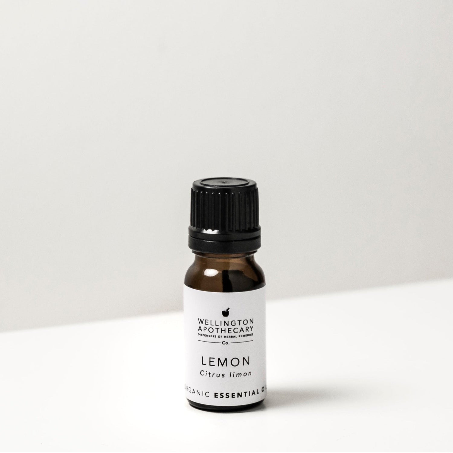 Small amber glass bottle of lemon essential oil on white bench. 