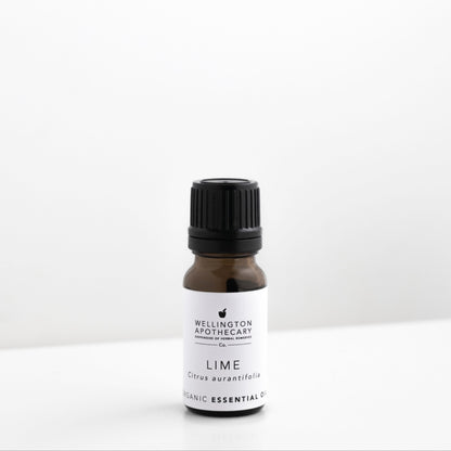 Small amber glass bottle of lime essential oil on white bench. 