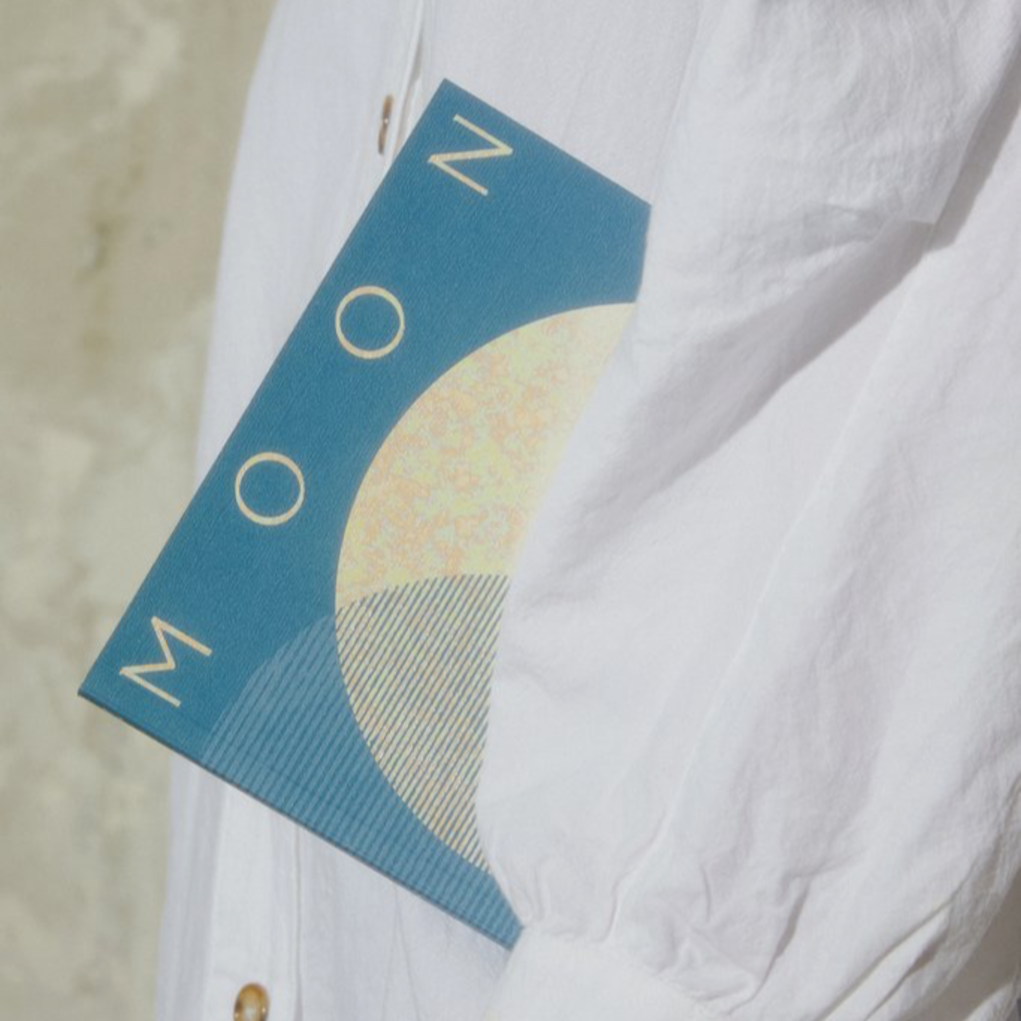 A woman in a white linen shirt carrying a Moon Lists journal under her arm. 