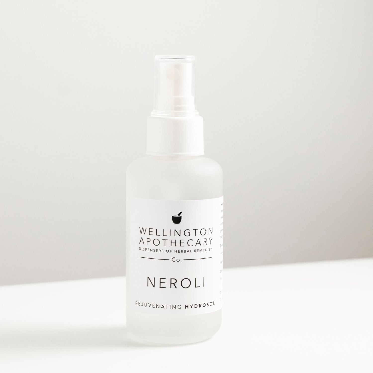 Frosted white glass bottle filled with neroli hydrosol, on white bench and soft grey background.