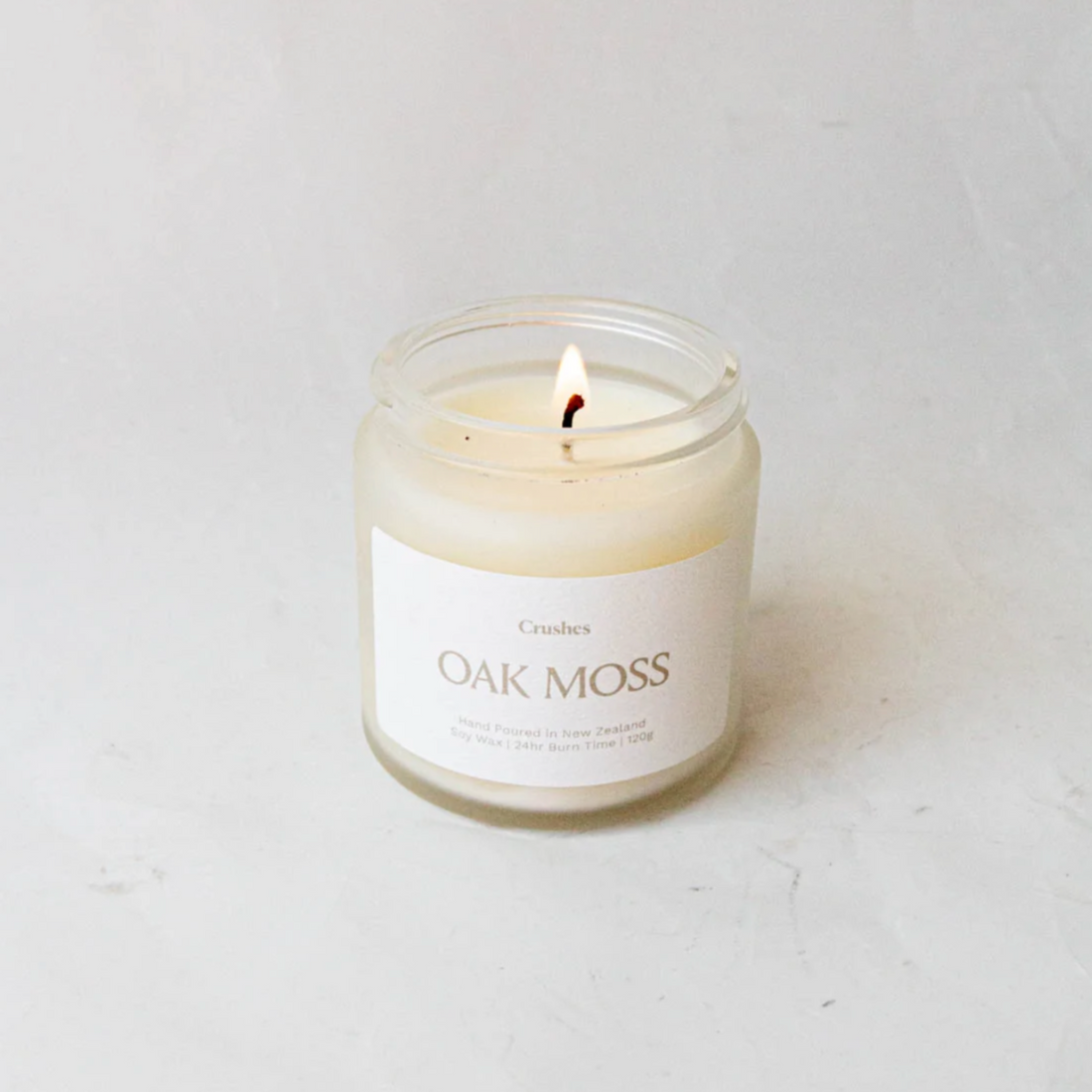 Clear glass jar containing oak moss candle  alight on white background. 