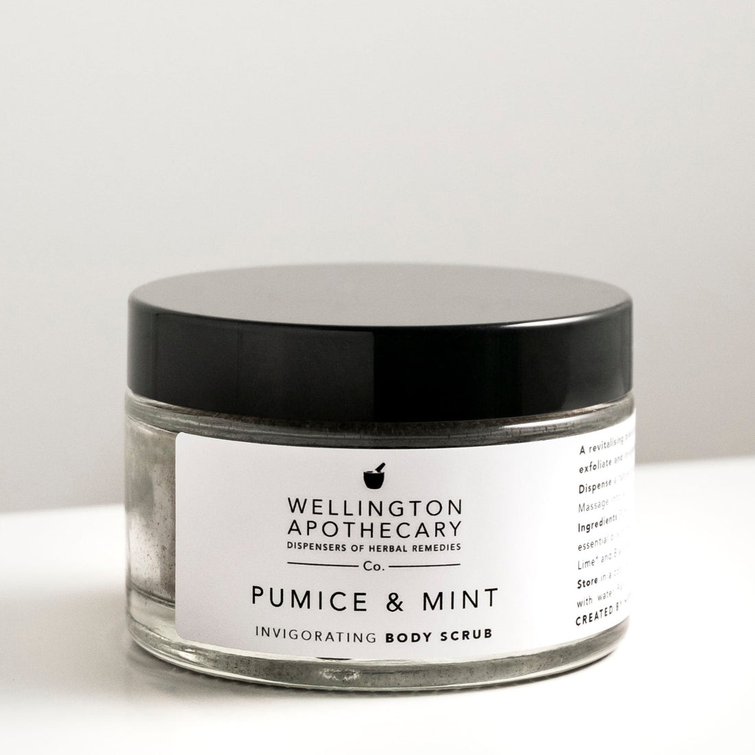 Large glass jar of pumice and mint body scrub on white bench. 