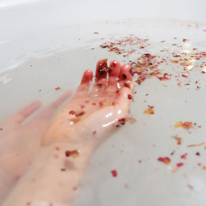 Rose petals in bath water with hands softly floating beneath the surface. 