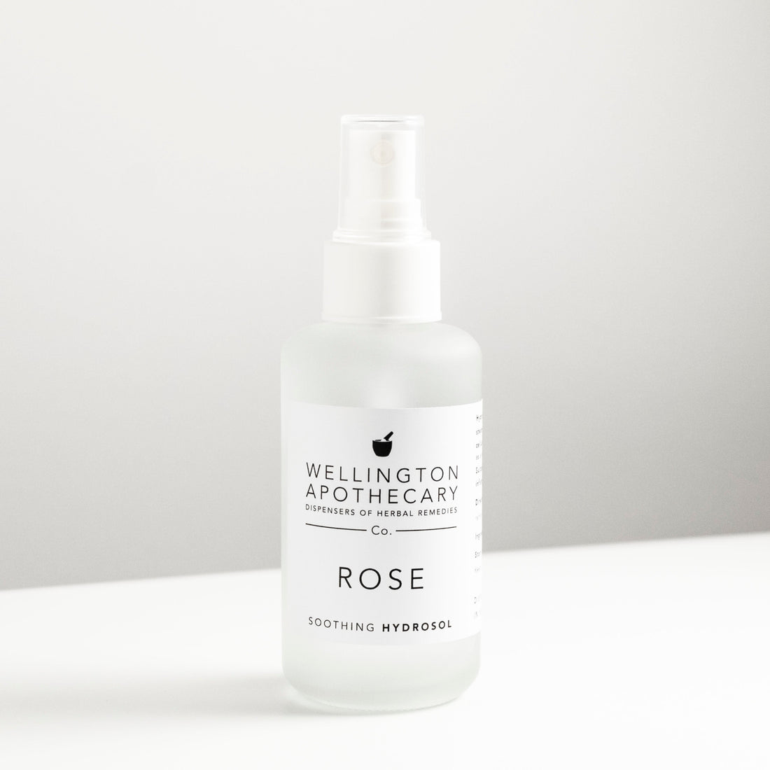 Clear glass spray bottle on white bench filled with rose hydrosol toner. 