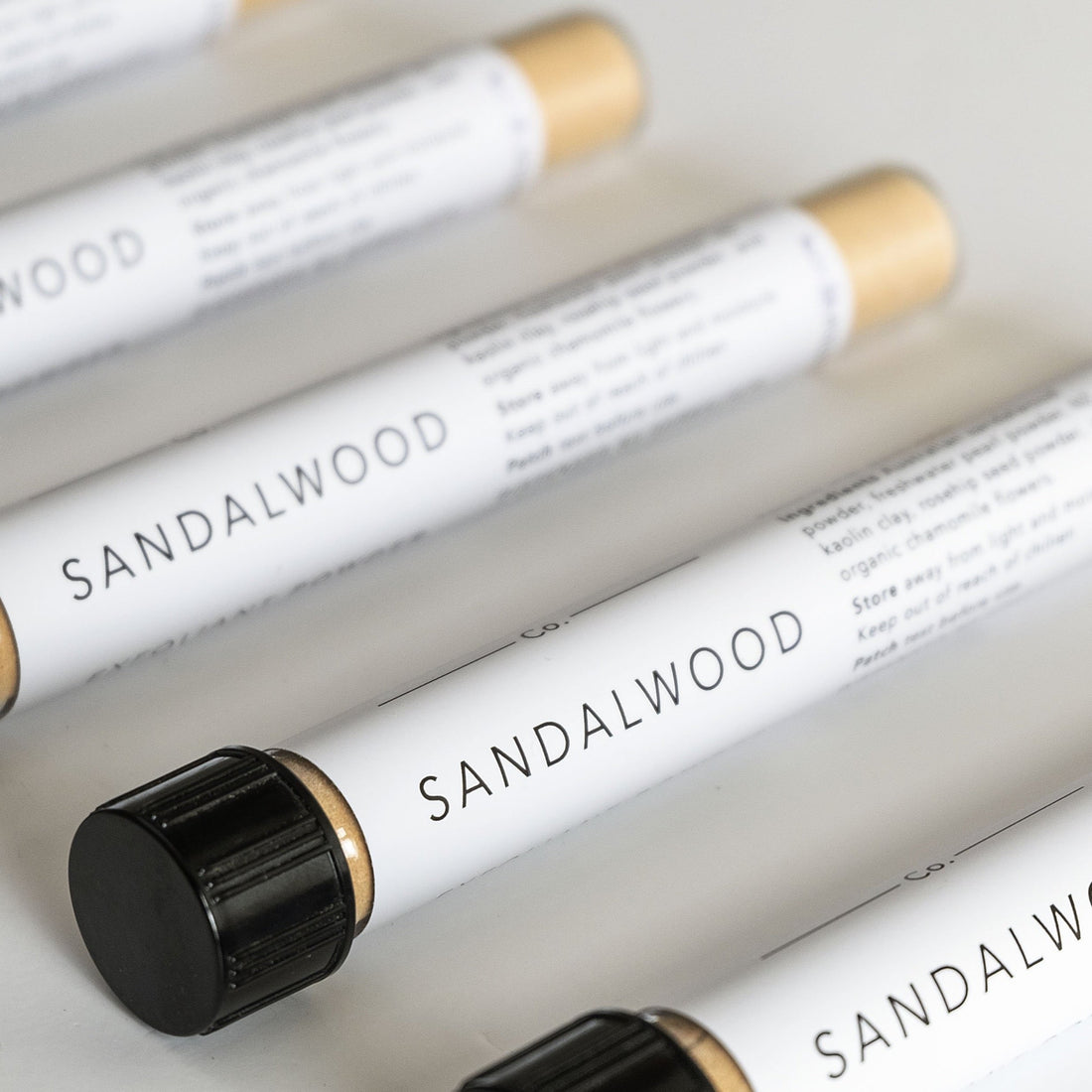 Glass test tubes lined up on white bench filled with sandalwood exfoliant powder blend. 