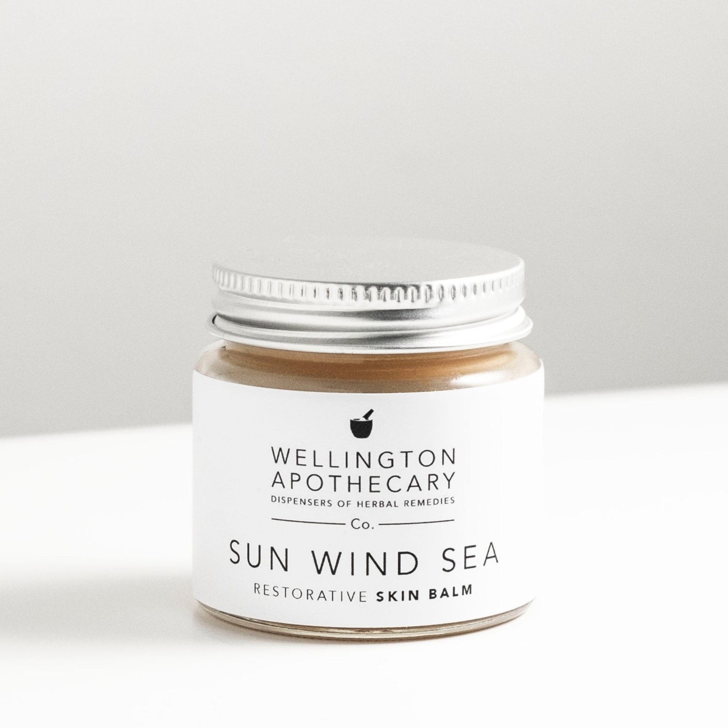 Glass jar of honey coloured sun wind sea balm on white bench. 