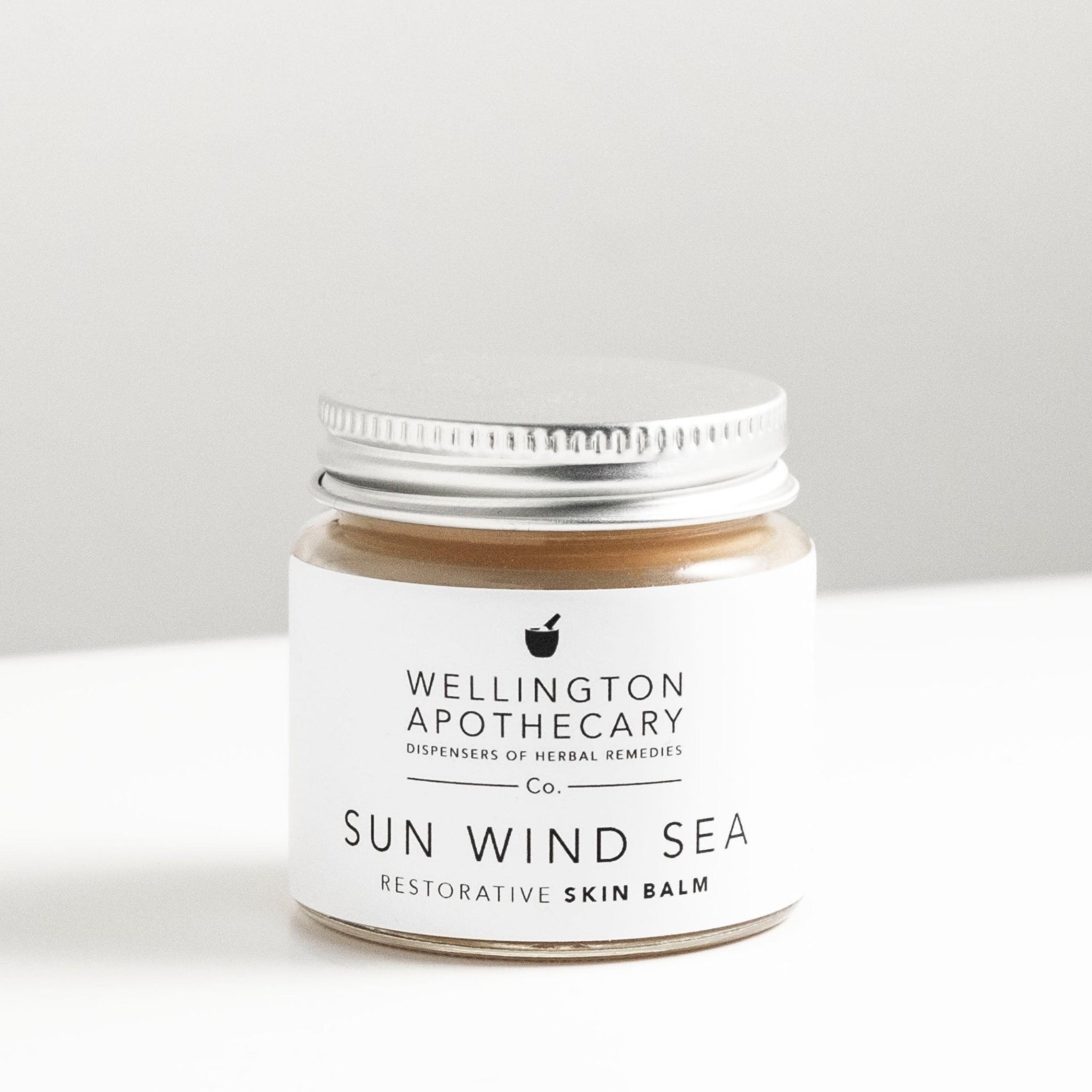 Glass jar of honey coloured sun wind sea balm on white bench. 