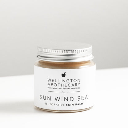 Glass jar of honey coloured sun wind sea balm on white bench. 