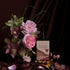 A bottle of sweet love tincture in a velvety maroon setting with roses, hellebore flowers and cinnamon quills.