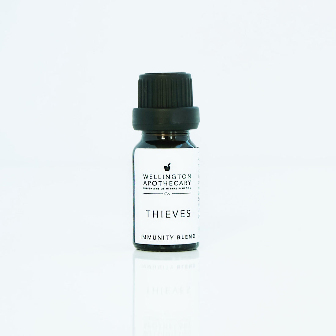 Small glass bottle with white label of thieves essential oil blend and black lid on white bench.