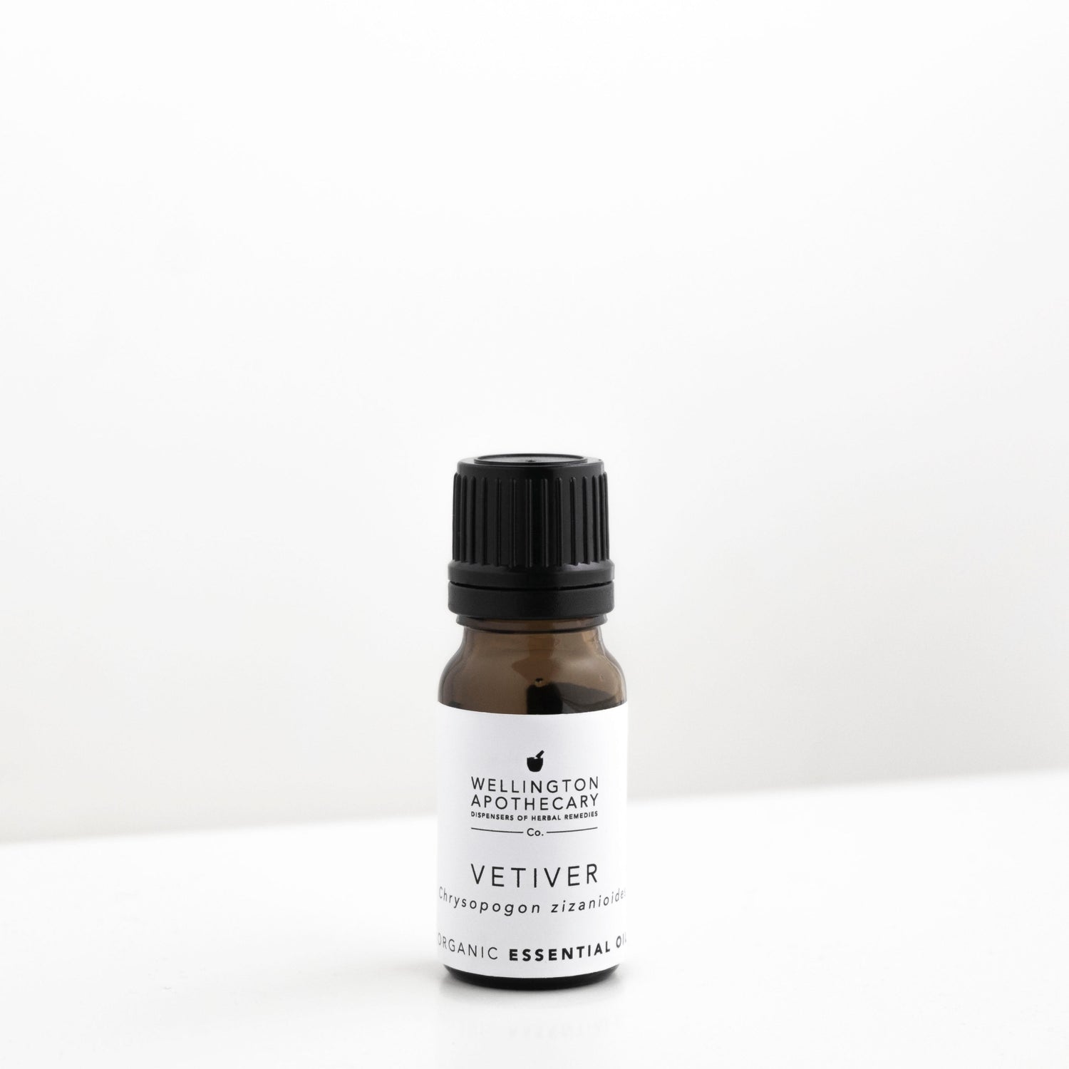 Small amber glass bottle of vetiver essential oil on white bench. 