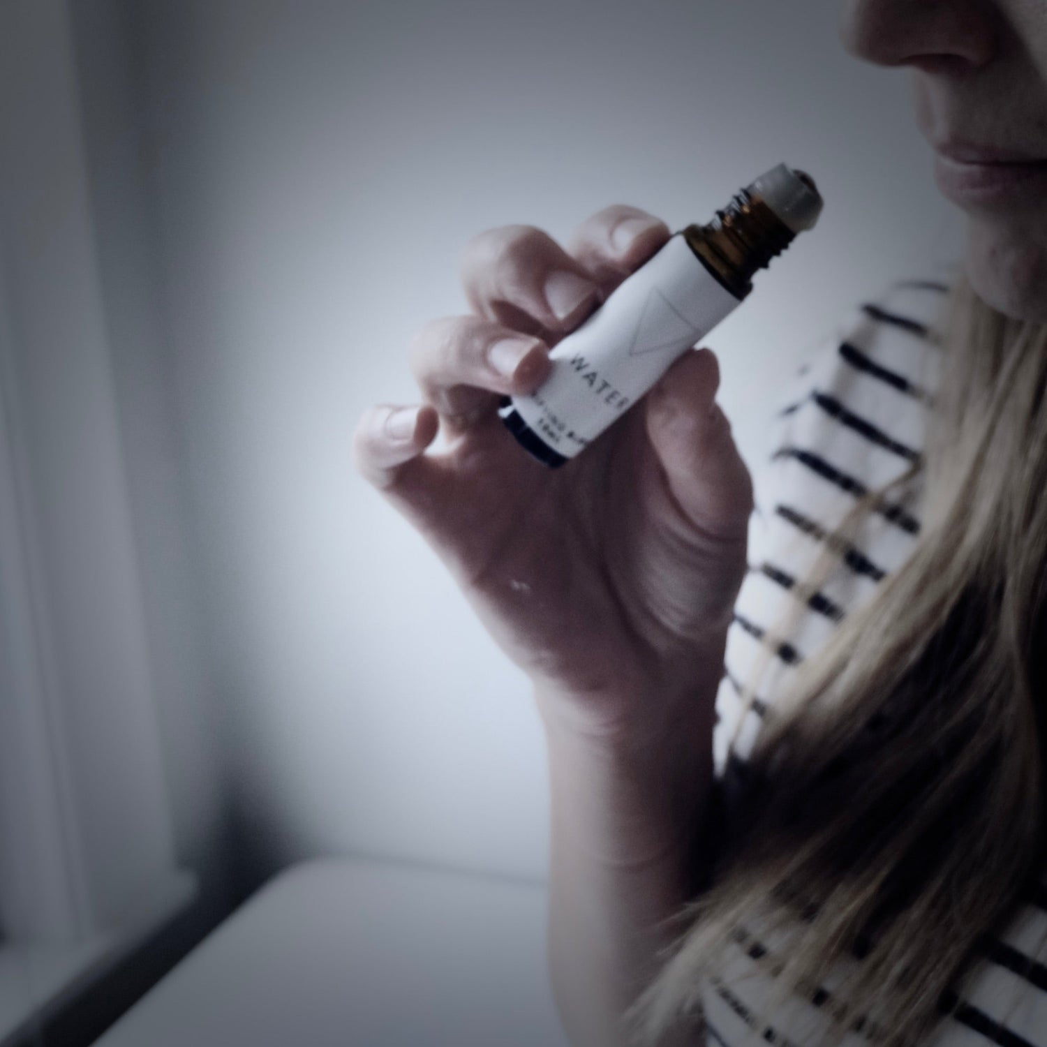 A woman inhaling the water blend of essential oils in a dimly lit bedroom. 